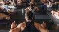 A yoga instructor leads a group yoga class, with participants in various poses on mats in a spacious, well-lit studio.