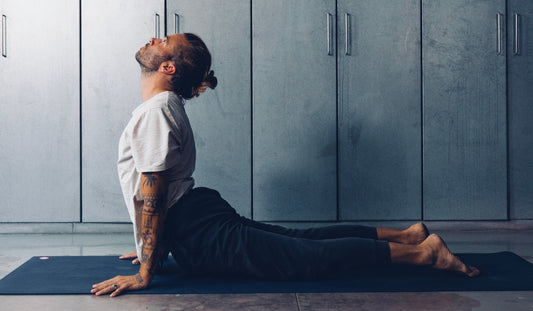 A person performs the upward-facing dog yoga pose on a blue mat, showcasing flexibility against a backdrop of gray cabinets.