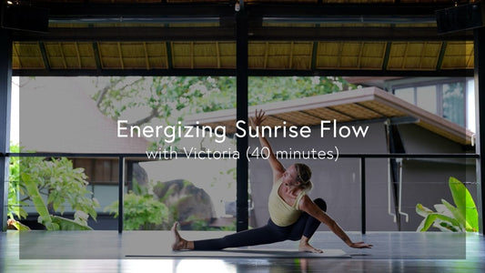 Woman performing a deep yoga stretch on a mat in a bright, open studio with tropical greenery outside.