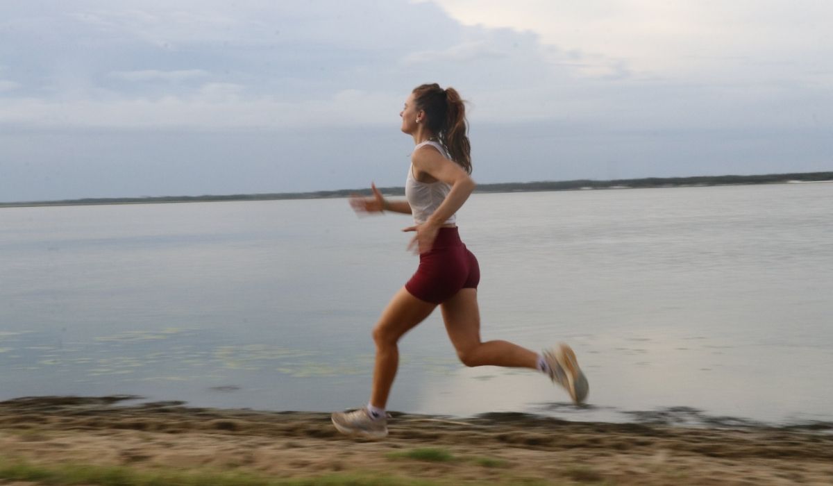 Woman in athletic wear running along a lakeside path under a cloudy sky during daytime.