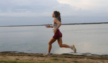 Woman in athletic wear running along a lakeside path under a cloudy sky during daytime.