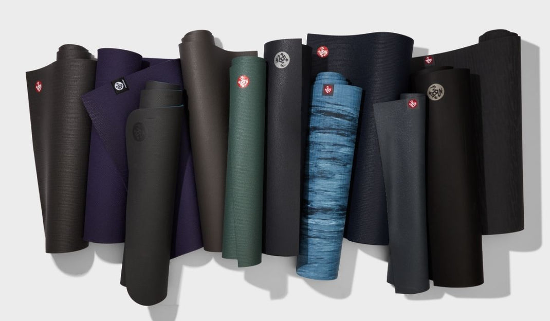 A collection of various yoga mats, rolled and displayed in different colors, including dark shades and a blue gradient.