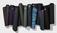 A collection of various yoga mats, rolled and displayed in different colors, including dark shades and a blue gradient.