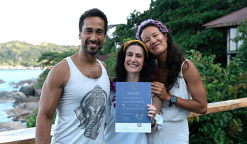 Three smiling people outdoors by water and greenery, one holding a certificate.