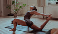 A person practicing yoga in a deep lunge pose, stretching gracefully on a mat in a serene, sunlit room with greenery.