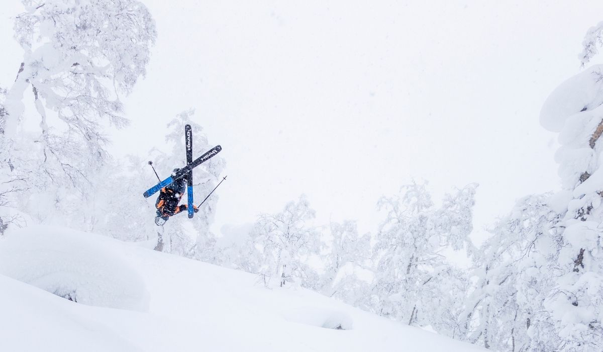 A skier performs a mid-air trick over a snowy slope, surrounded by frost-covered trees in a winter wonderland.