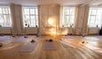 A serene yoga studio with wooden floors, multiple mats, yoga blocks, and natural light streaming through large windows.