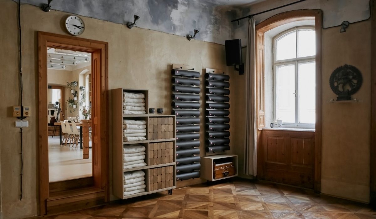 Cozy room with wooden parquet, shelves of folded blankets and boxes, yoga mats on wall racks, a large window, and an open door to a dining area.
