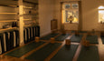 Serene yoga studio with wooden shelves, mats, blocks, and candles, bathed in warm afternoon light. Window features decorative elements.
