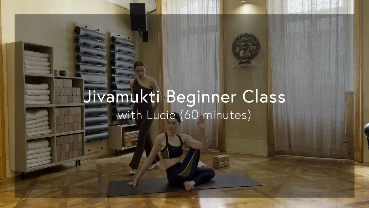 Two women practicing yoga in a bright studio with wooden floors, towels, and yoga props neatly arranged on shelves.