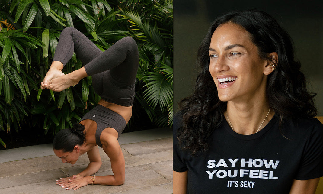 A woman performs a yoga pose, balancing on her hands with legs raised, surrounded by lush green foliage.