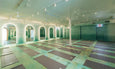 Yoga studio with multiple gray mats neatly arranged on a green floor, arched mirrors with glowing backlights, and ceiling fans.