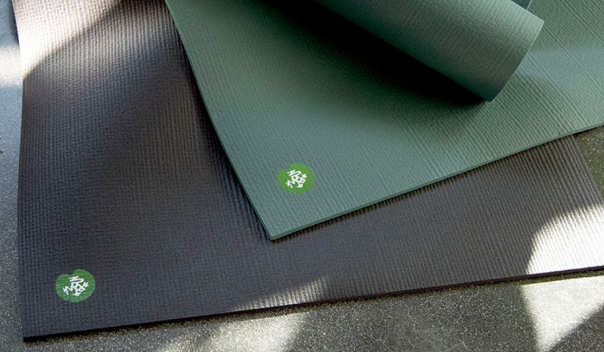 Two yoga mats in dark gray and green with textured surfaces, featuring a small green logo in the corner.