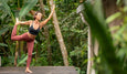 A person practicing yoga in a balanced pose on a wooden platform surrounded by lush greenery.