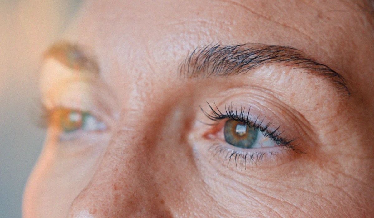 Close-up of a person's eye and eyelashes, showcasing clear skin texture and a hint of light reflecting in the eye.