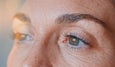 Close-up of a person's eye and eyelashes, showcasing clear skin texture and a hint of light reflecting in the eye.