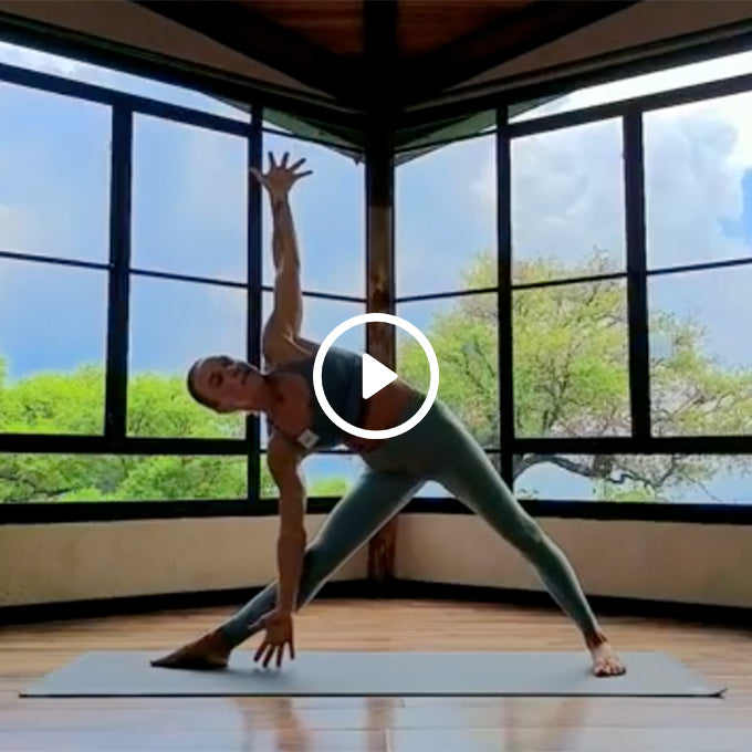 Person practicing yoga in a spacious room with large windows, performing a side triangle pose on a mat.