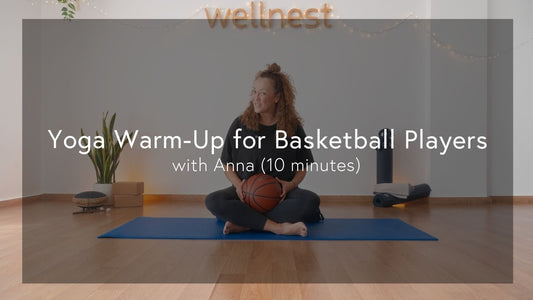 A person sits cross-legged on a blue yoga mat, holding a basketball, in a serene, well-decorated wellness space.