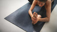 A person stretches on a black yoga mat, grasping their foot with both hands, focusing on flexibility and balance.