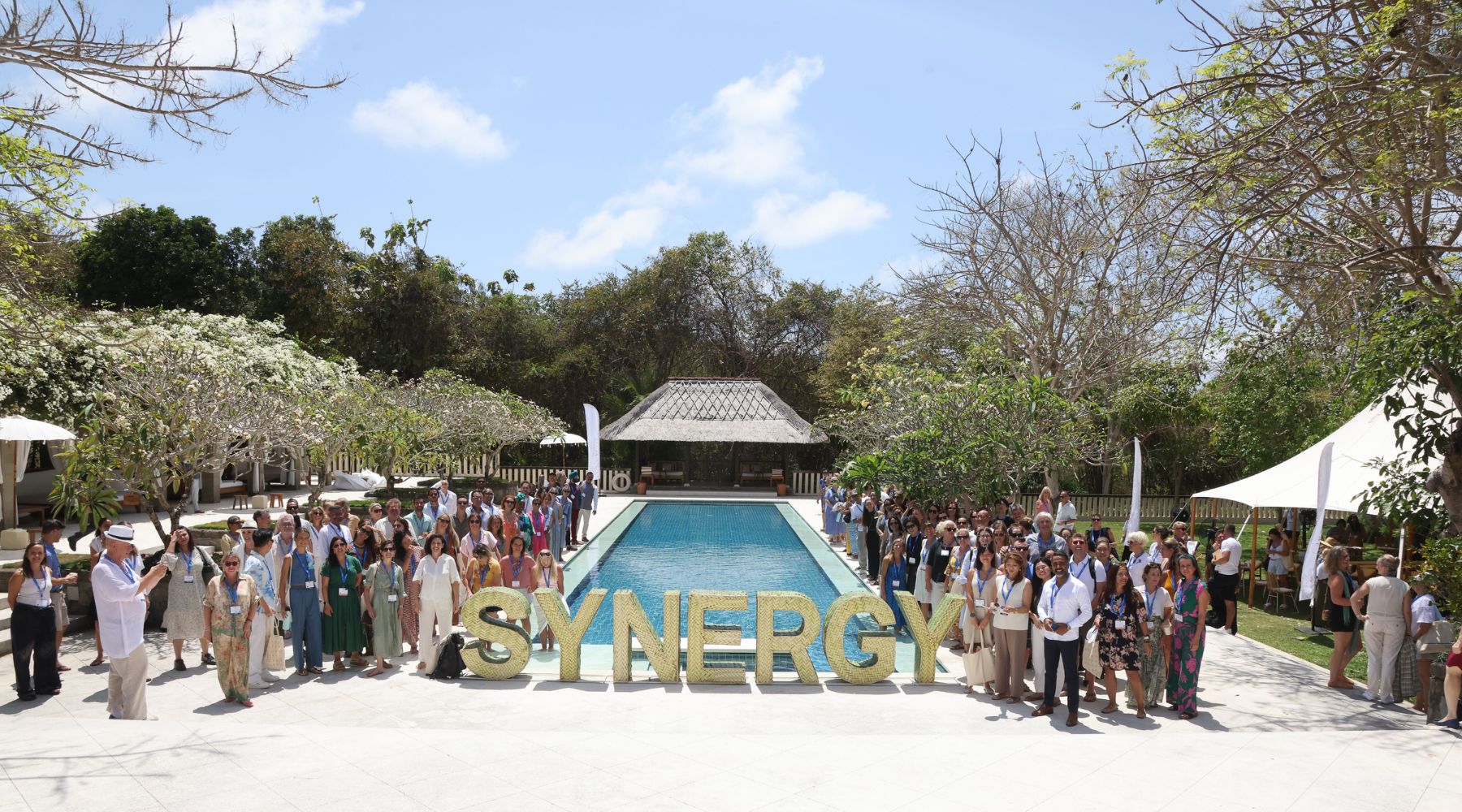 A large group of people stands beside a pool, with a decorative 