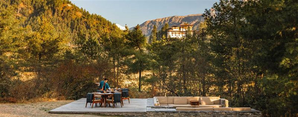 Outdoor setting with a table and chairs surrounded by trees and mountains.